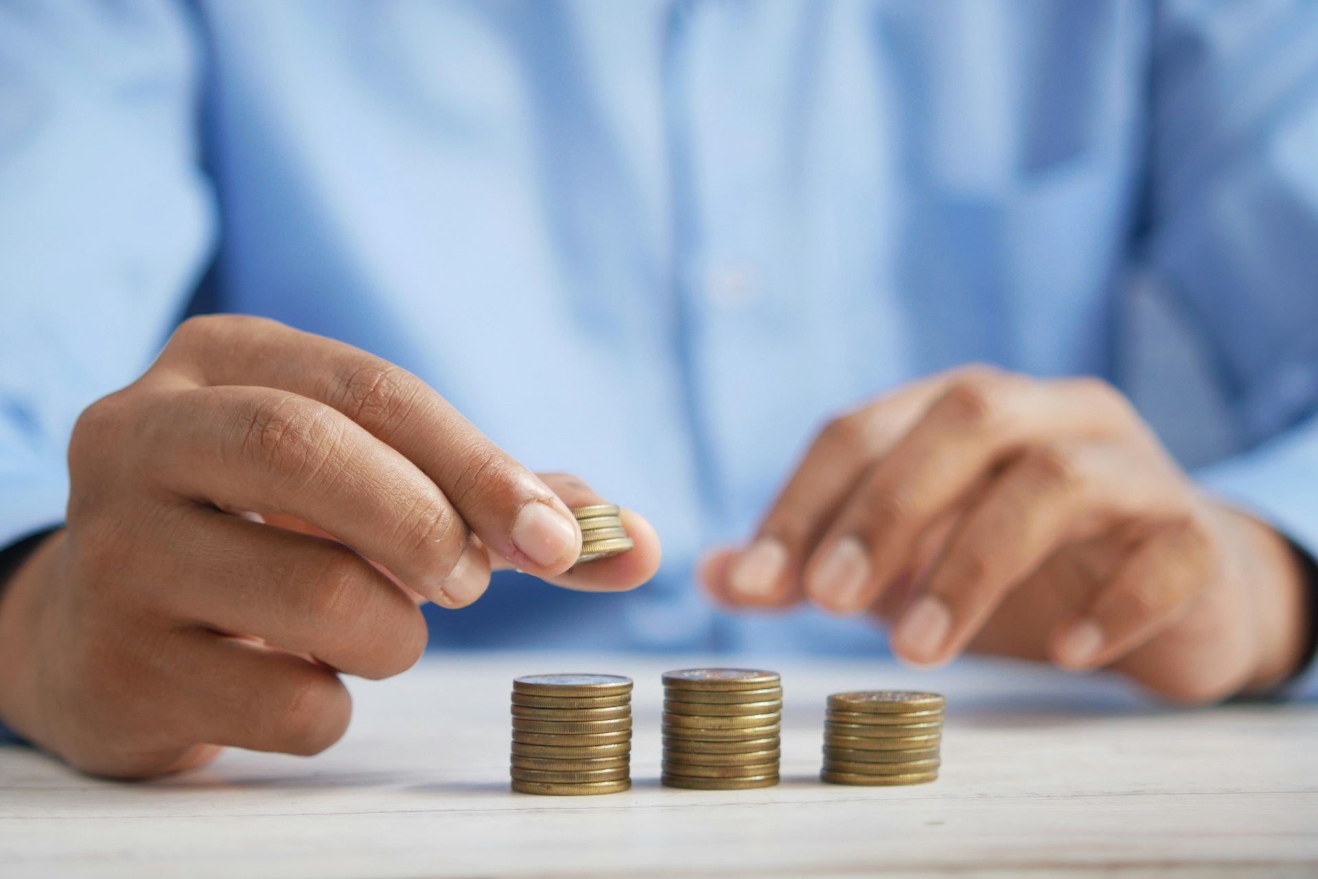 a man with blue shirt is budgeting and stacking coins