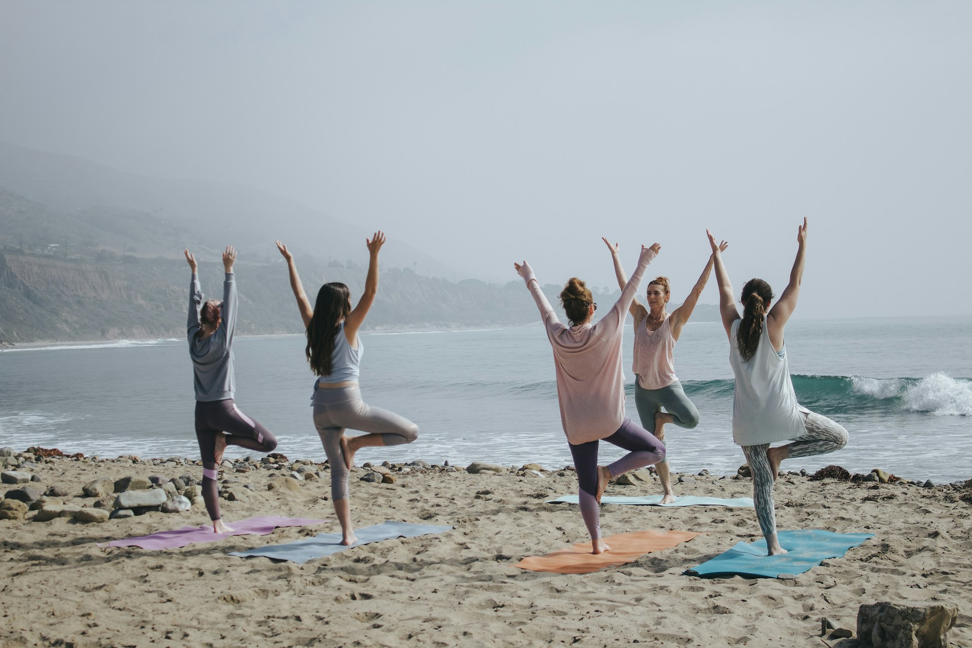 five people doing yoga near the beach